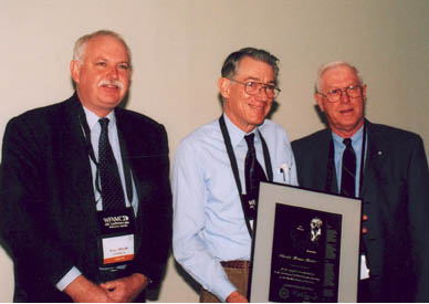 Harold Reiter (centre) receives his Paul Erdös Award from WFNMC President Peter Taylor (left) and WFNMC Awards Committee Chairman Ron Dunkley (right). The presentation took place on Saturday 10 August 2002, at the Ibis Hotel, Melbourne, as part of WFNMC's 4th conference.